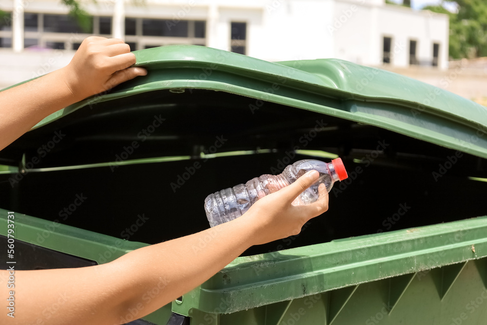 Child throwing plastic bottle into garbage container outdoors, closeup