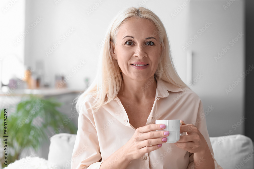 Mature woman with cup of hot beverage sitting on sofa at home, closeup