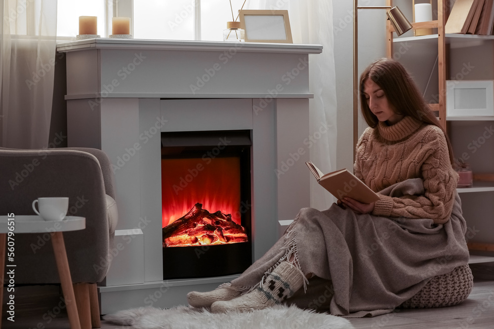 Young woman reading book near fireplace in living room