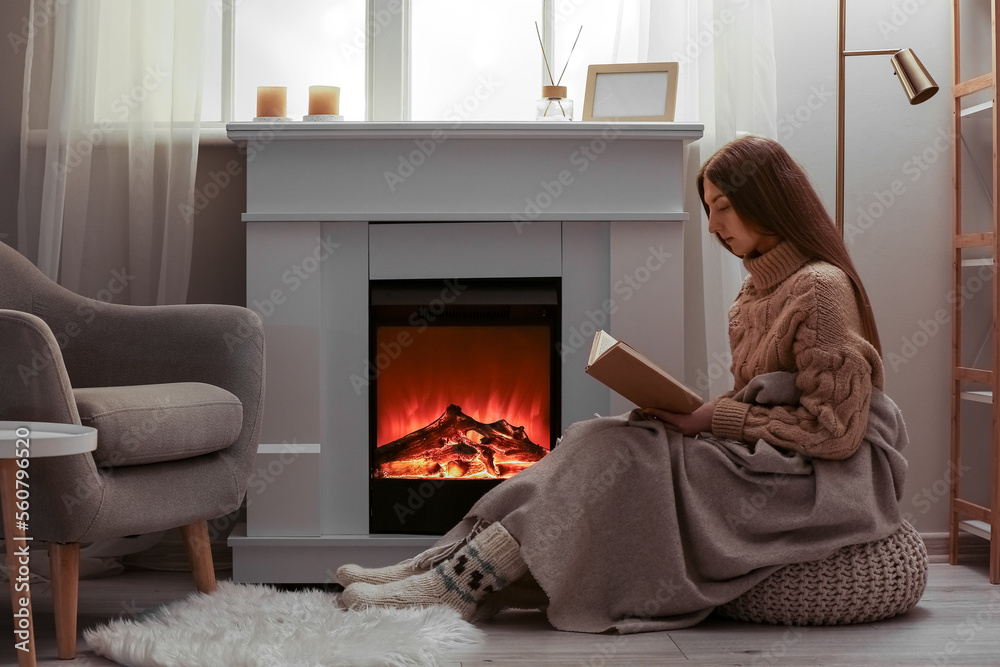 Young woman reading book near fireplace in living room