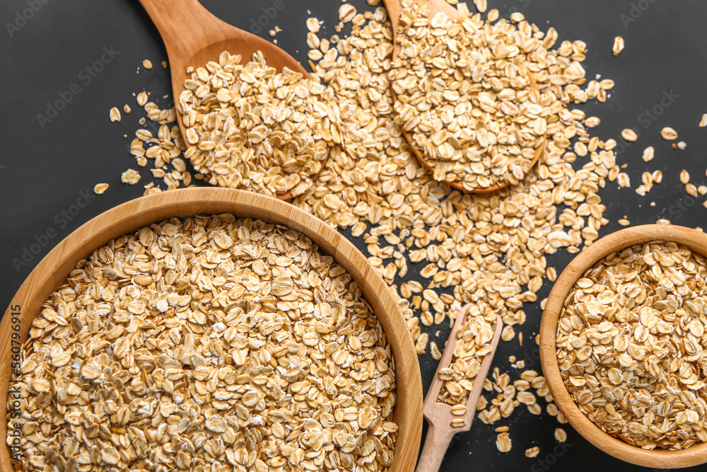 Bowls and spoons of raw oatmeal on dark background, closeup