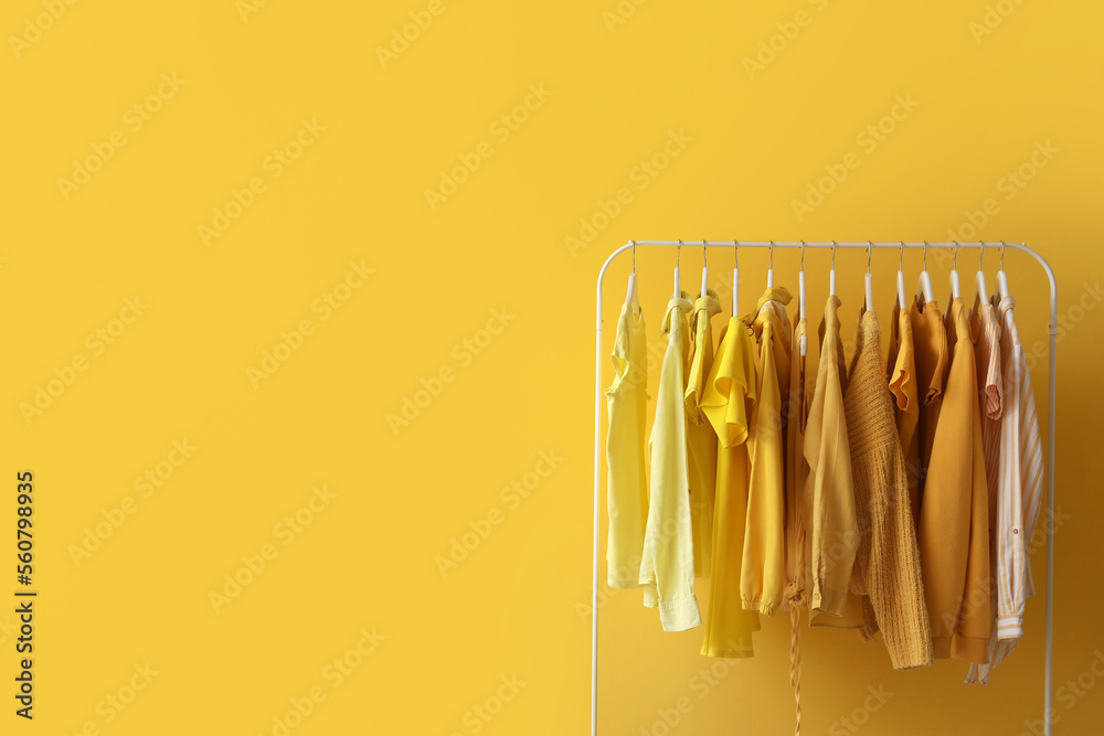 Rack with stylish female clothes near yellow wall