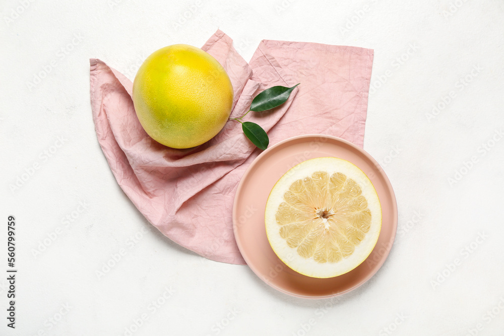 Plate with pomelo fruit and pink kitchen towel on light background