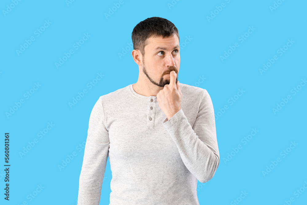 Handsome man biting nails on blue background