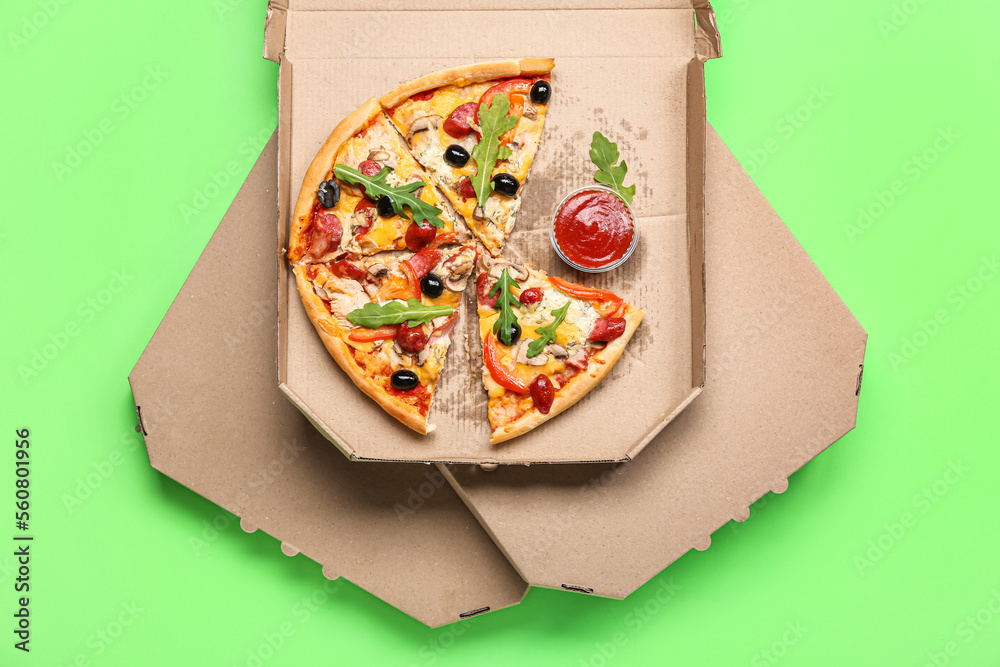 Stack of cardboard boxes with tasty pizza and sauce on green background