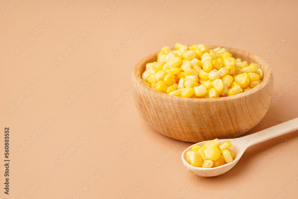 Bowl and spoon with canned corn kernels on beige background