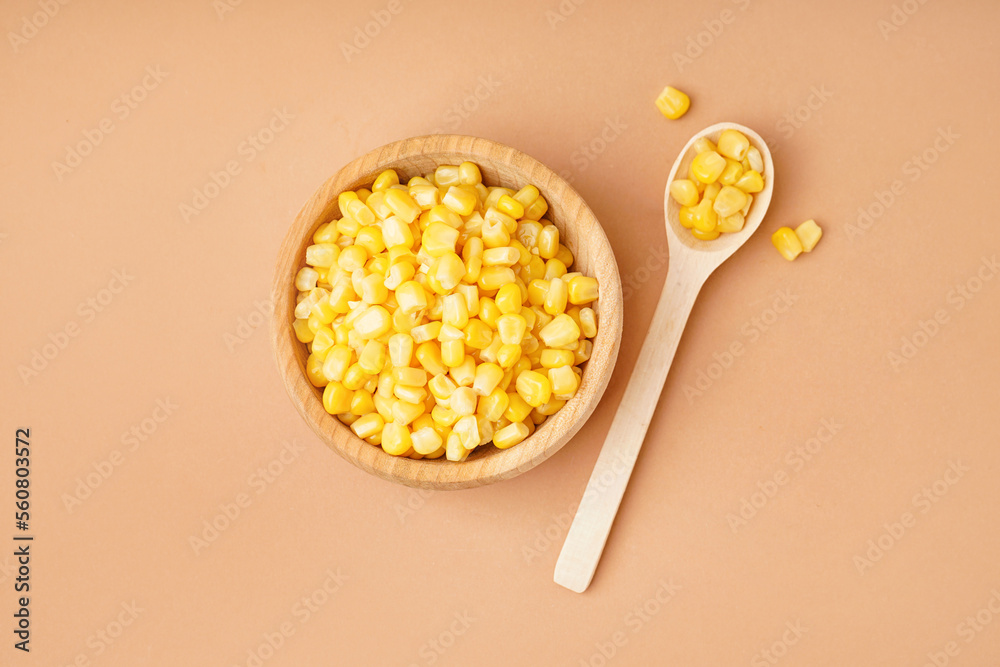 Bowl and spoon with canned corn kernels on beige background