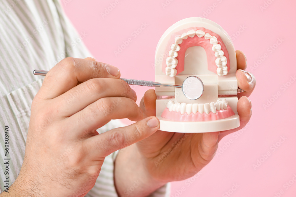 Young man with jaw model and dental tool on pink background, closeup