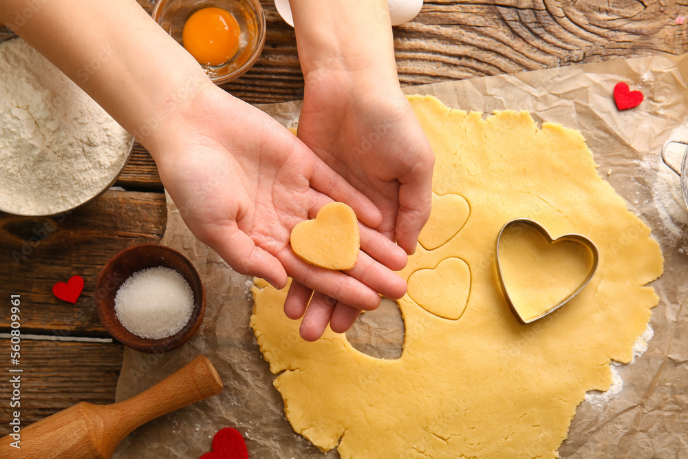 Female hands with raw cookie, dough, sugar and cutter on wooden background. Valentines Day celebrati