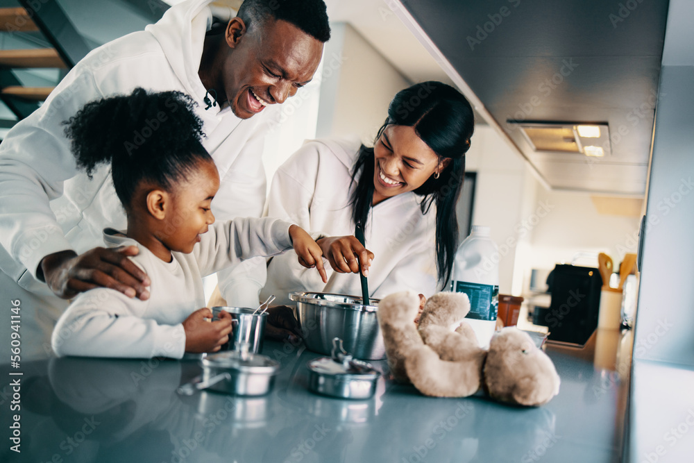 Parents making pancakes with their little daughter in the kitchen; black family preparing breakfast 