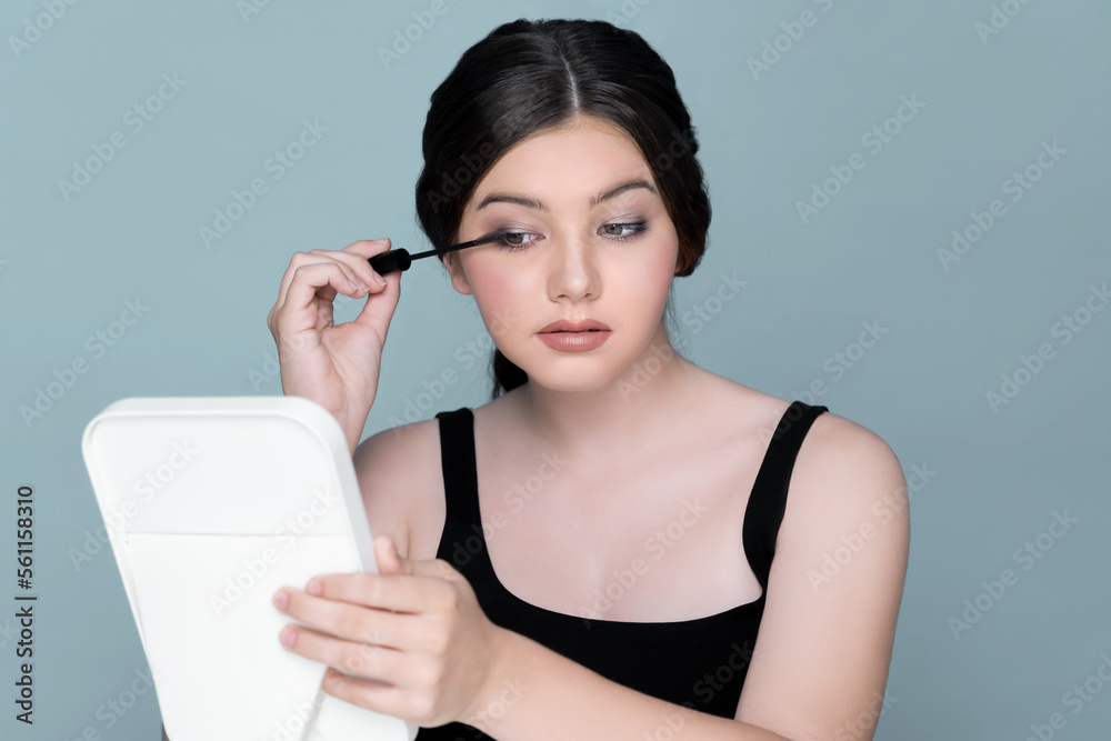 Beauty portrait of young girl applying eye mascara, eye makeup in front of mirror. charming young br