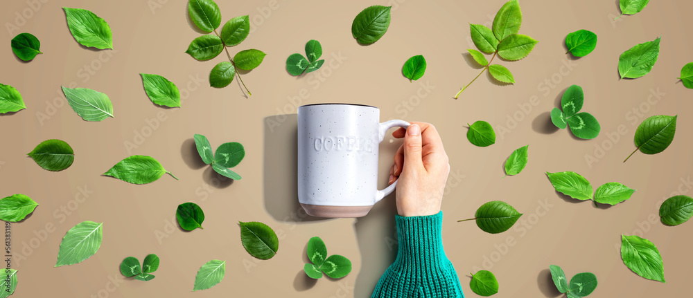 Person holding a mug with green leaves - flat lay