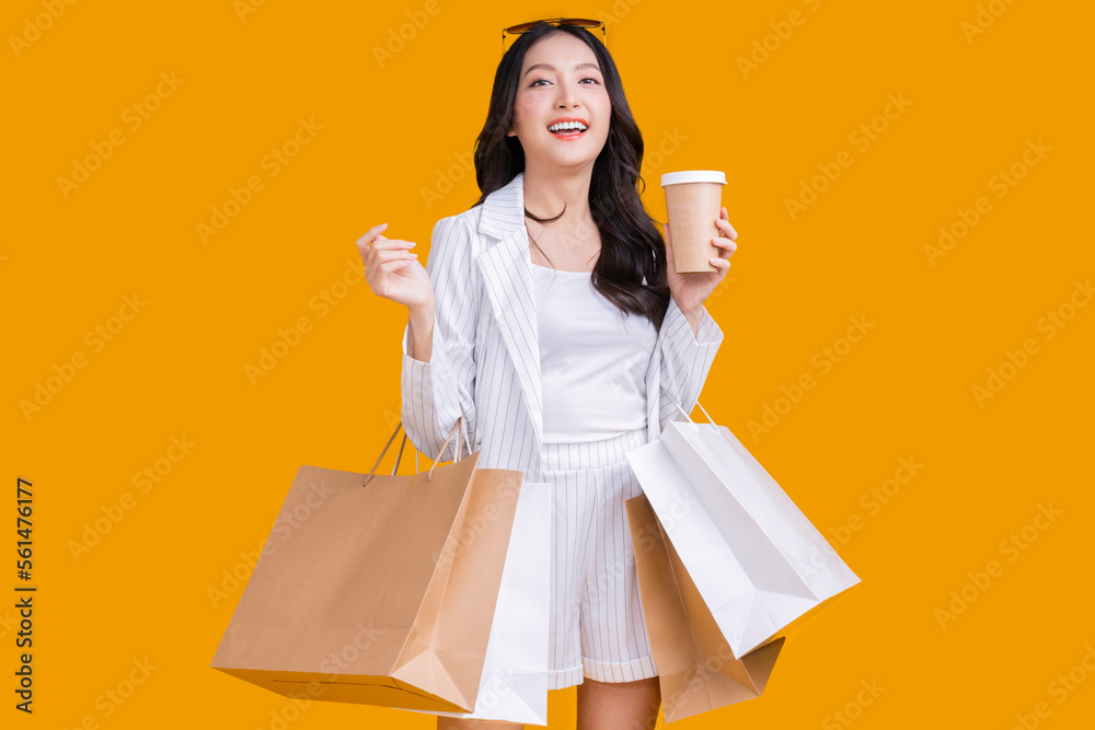 Asian happy female woman girl holds colourful shopping packages   standing on yellow background stud