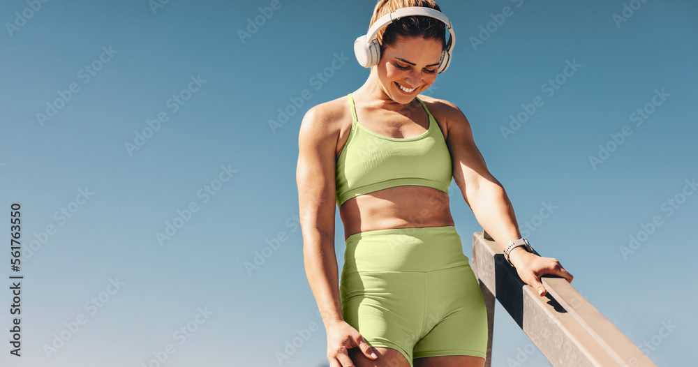 Smiling fit woman in sportswear, earphones in and enjoying the sunny day while exercising fitness ou