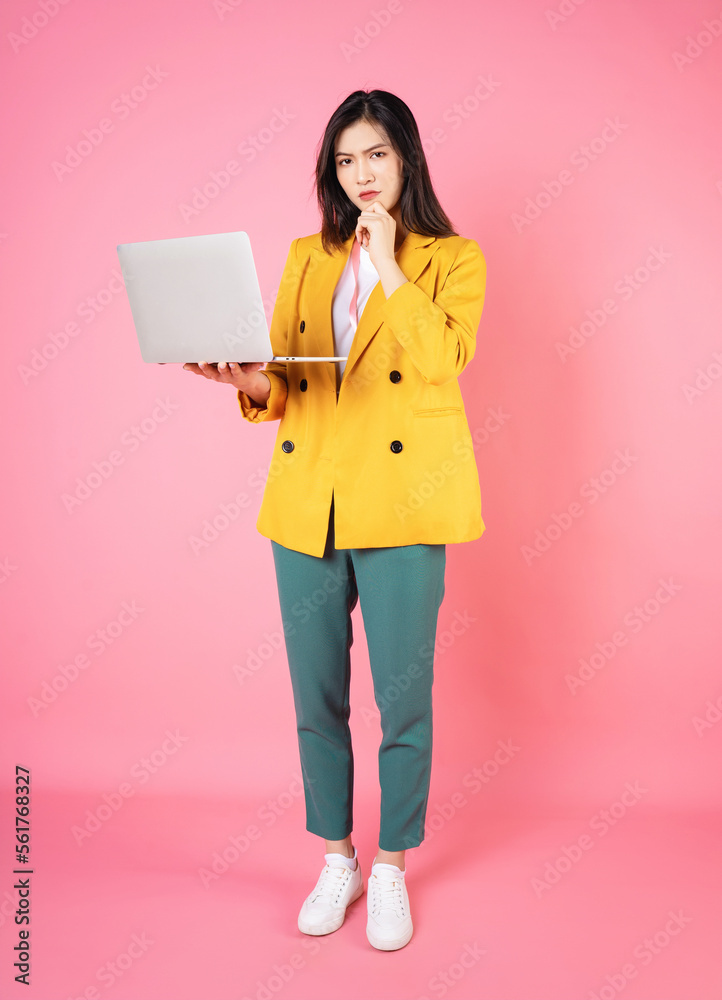 Full length image of young Asian bussinesswoman holding laptop on background