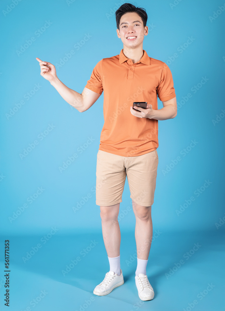 Image of young Asian man holding smartphone on blue background