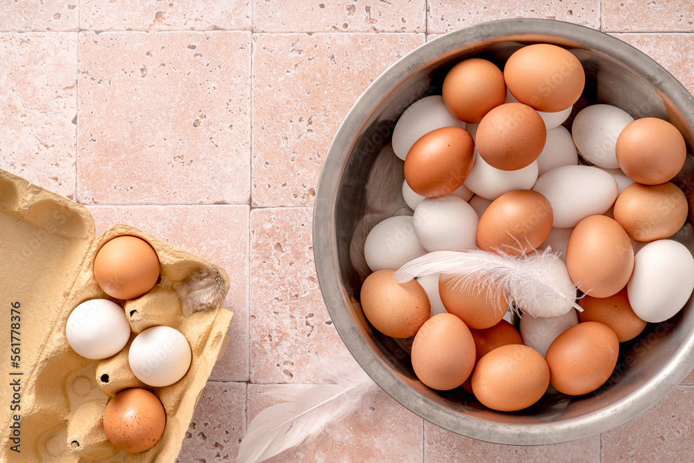 Eggs in metallic bowl on beige background. Top view of raw brown eggs and white eggs in open egg box