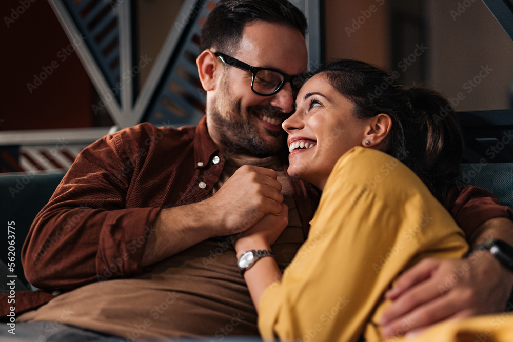 Two lovers holding hands, sitting closely to each other, smiling.