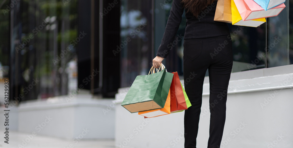 Young beautiful Asian woman holding colorful shopping bags walking on a city street. Happy woman wit