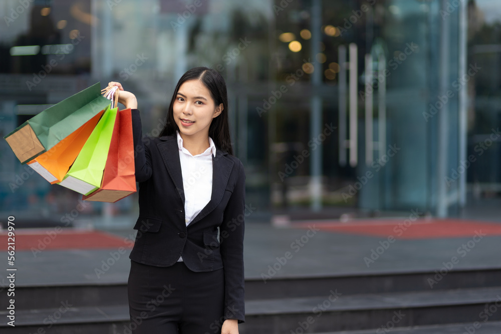 年轻漂亮的亚洲女人拿着五颜六色的购物袋在城市里行走。有shopp的快乐女人