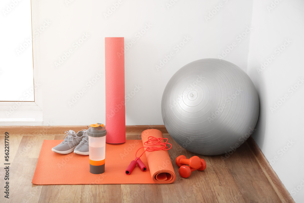 Sports water bottle with equipment and sneakers on mat near light wall