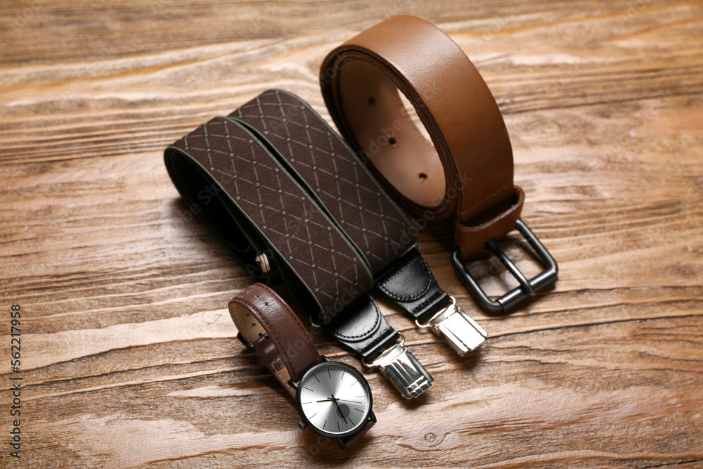 Male wristwatch, suspenders and leather belt on wooden background