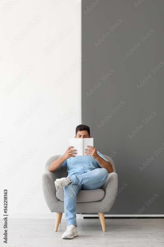 Handsome man reading book in armchair near black and white wall