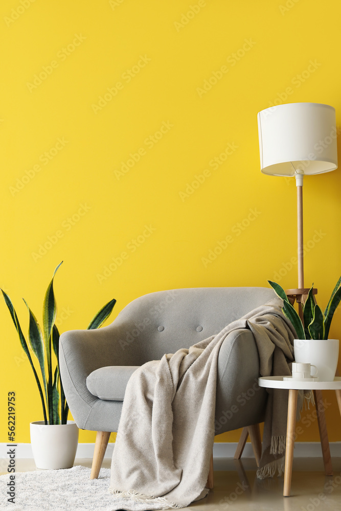 Grey armchair, table with houseplants and lamp near yellow wall