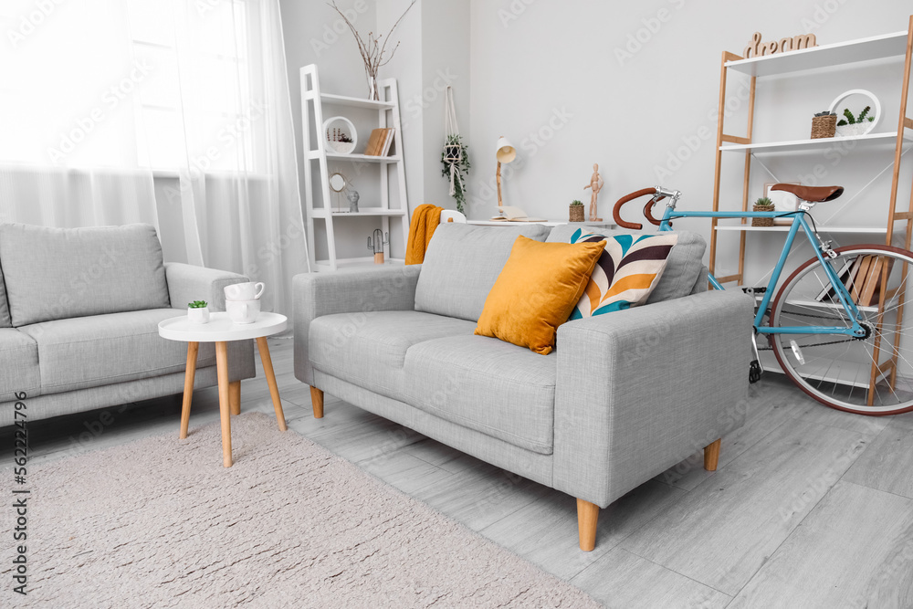 Interior of living room with grey sofas, coffee table, shelving units and bicycle near window