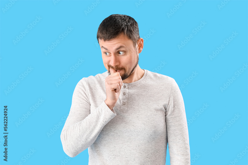 Handsome man biting nails on blue background