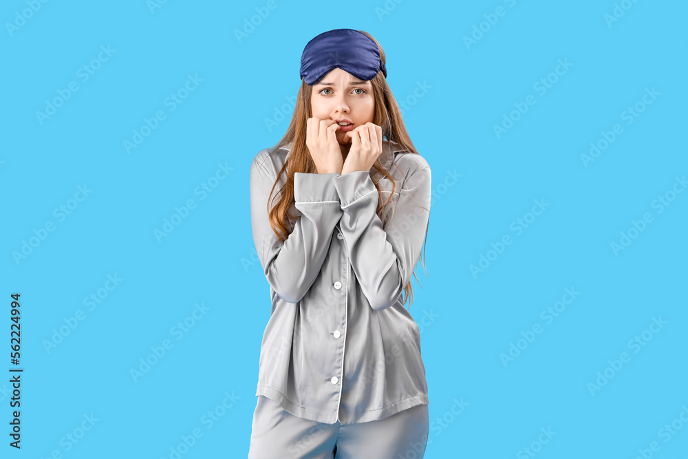 Young woman in pajamas biting nails on blue background