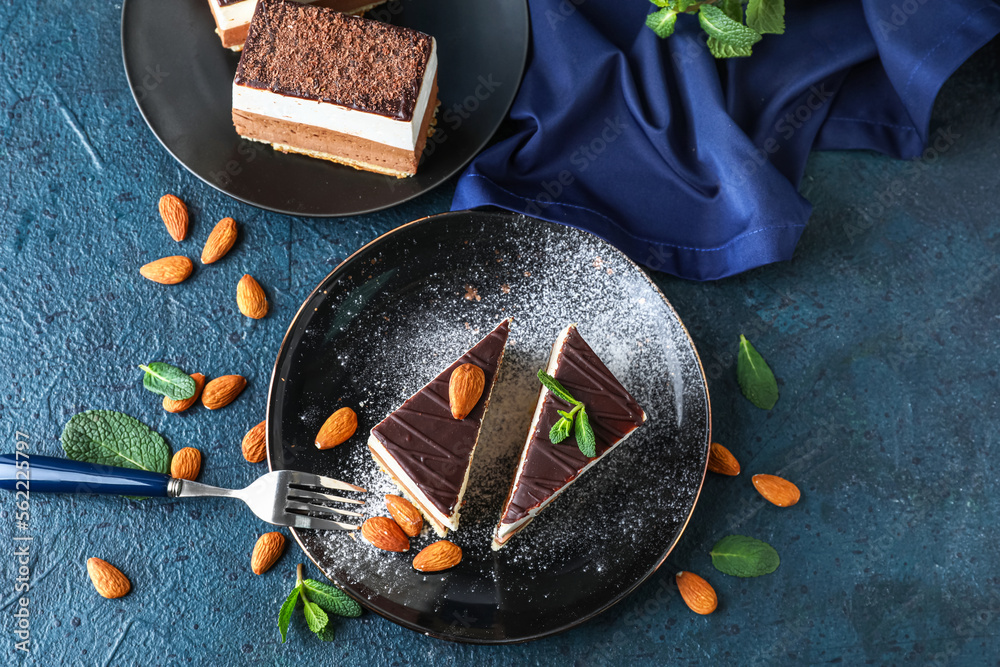 Plates with pieces of birds milk cake, almond nuts and mint leaves on blue table