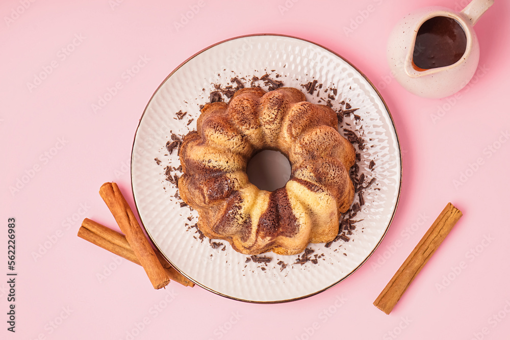 Plate with delicious cake, cinnamon and jug of hot chocolate on pink background