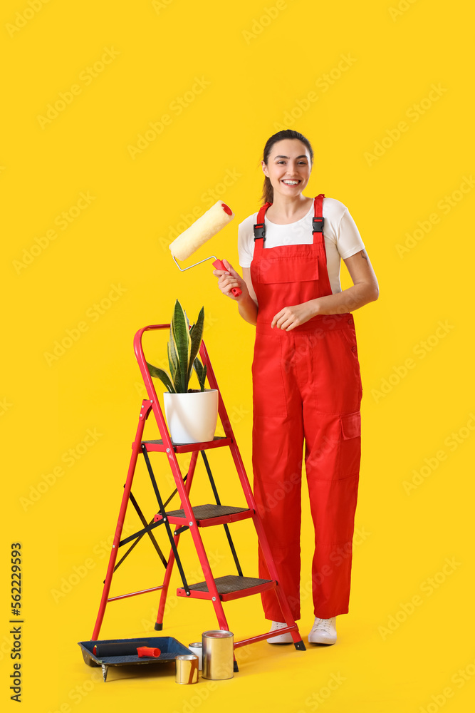 Young woman with roller, ladder, houseplant and paint cans on yellow background