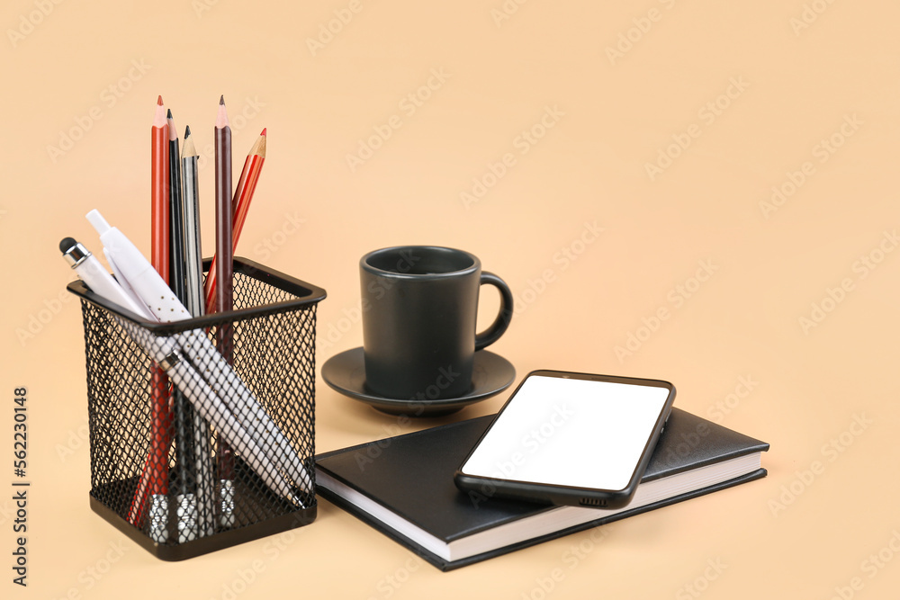 Stationery holder, mobile phone, notebook and cup of coffee on beige background