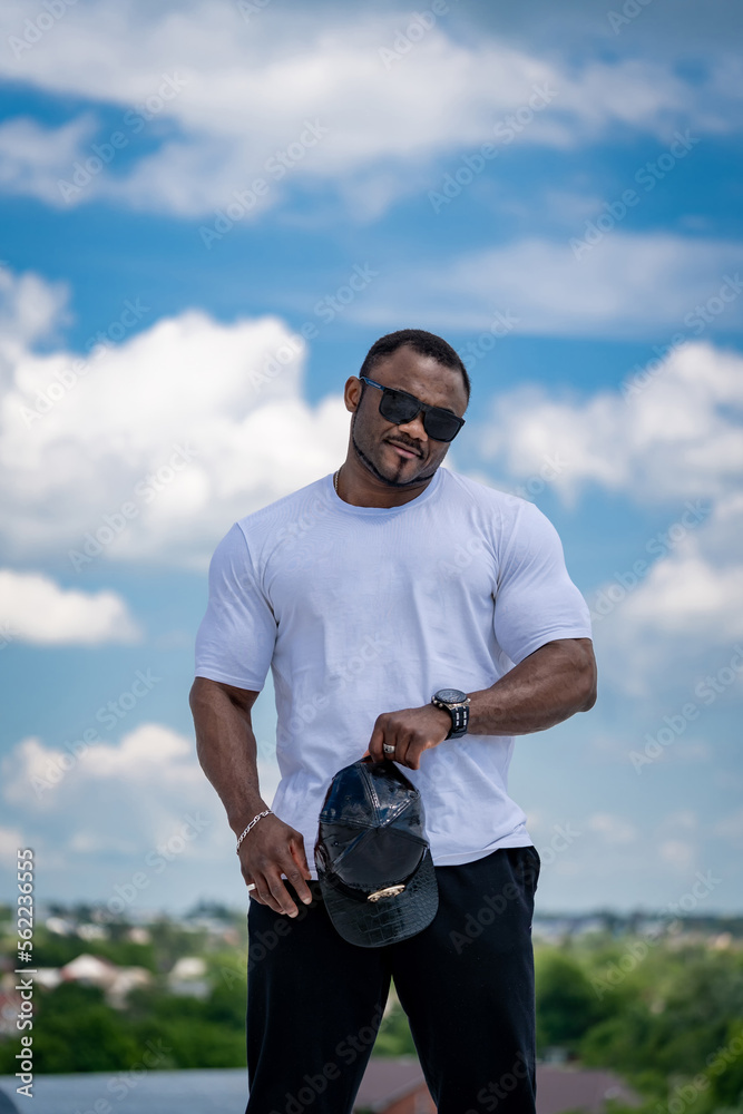 Strong big man in sunglasses outdoor. Handsome athletic man in white shirt standing outdoor.