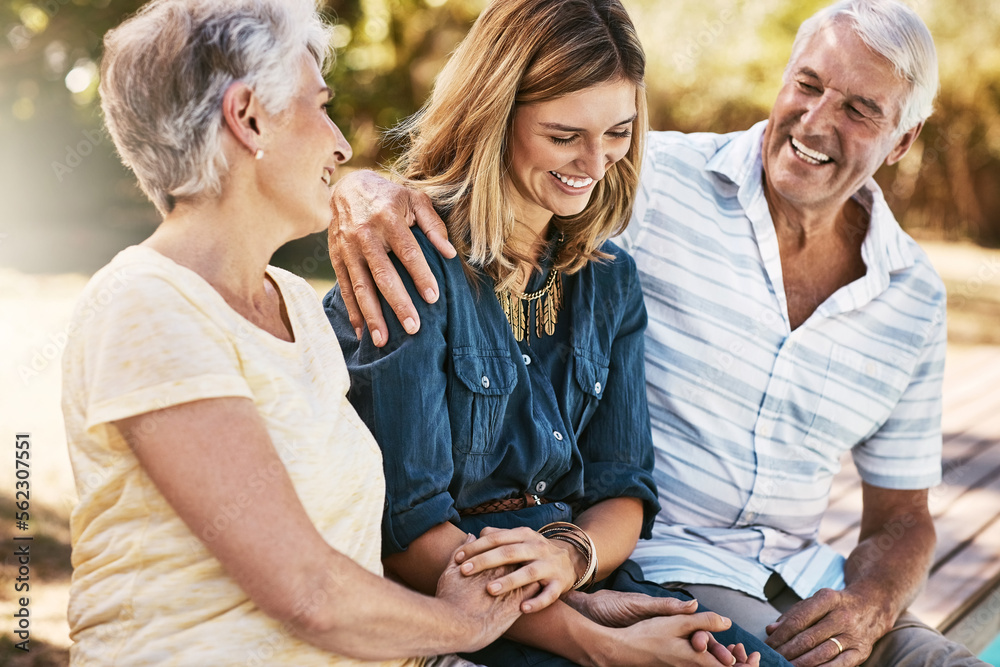 Senior couple in nature with their adult daughter sitting, talking and bonding together in a garden.