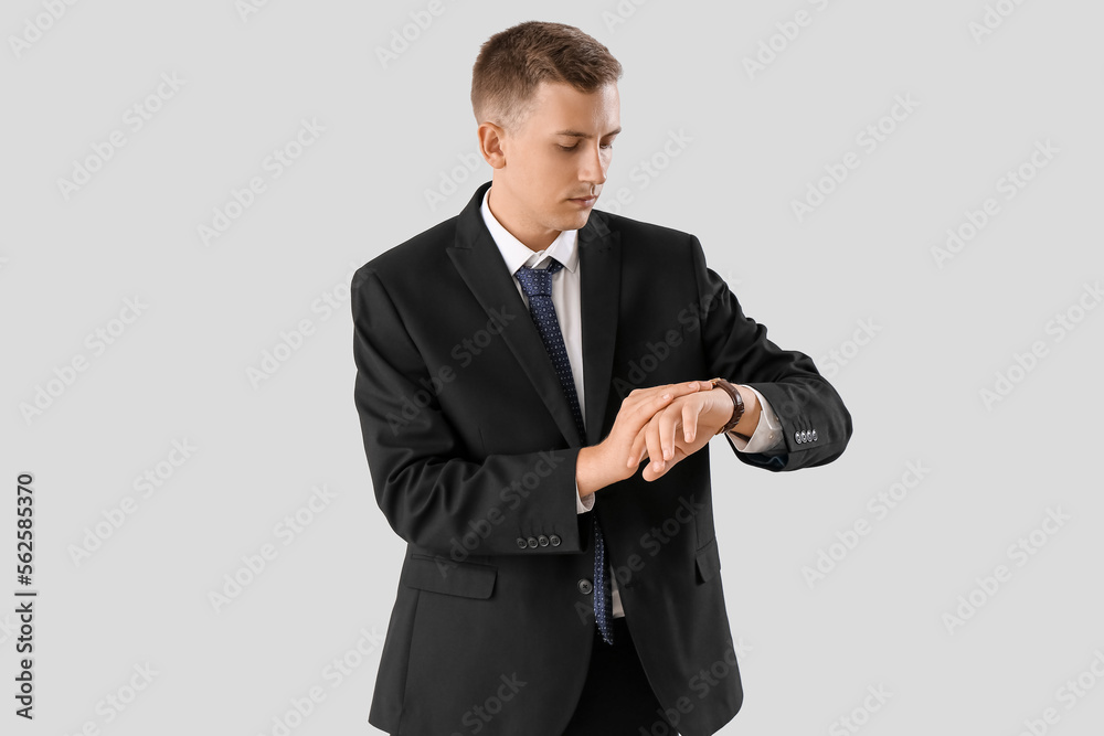 Handsome businessman looking at wristwatch on light background