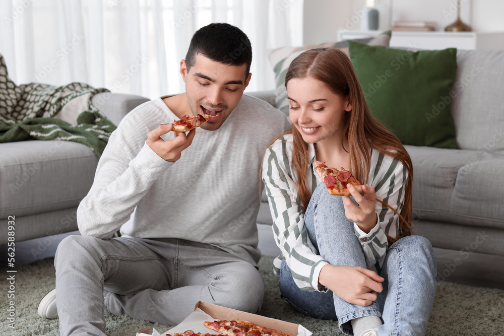 Happy young couple eating tasty pizza at home