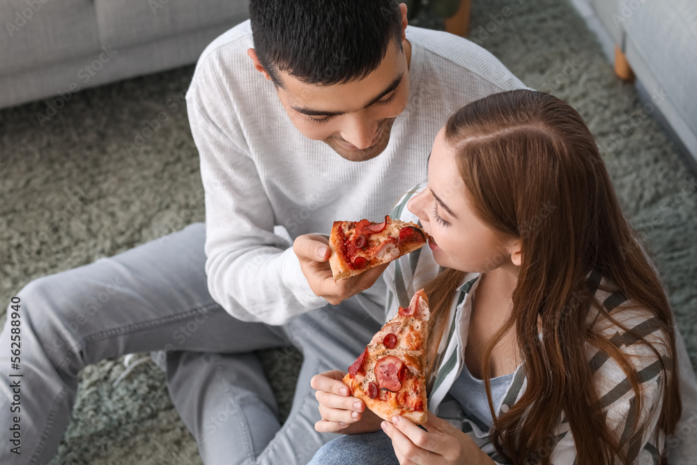 Happy young couple eating tasty pizza at home