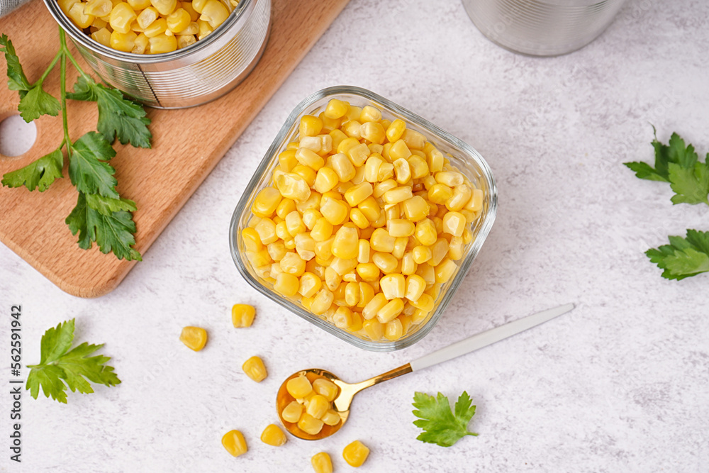 Bowl with corn kernels, cutting board, spoon and parsley on white table