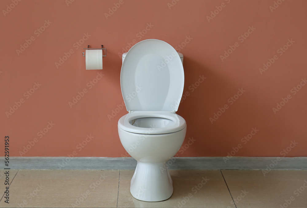 Ceramic toilet bowl and paper roll near pink wall