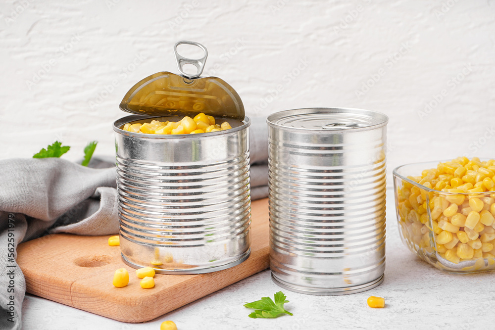 Tin cans, bowl of corn kernels, cutting board and napkin on grey table