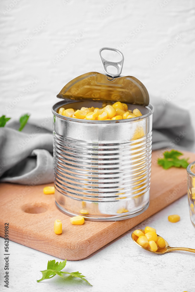 Board with tin can, corn kernels and parsley leaf on grey table