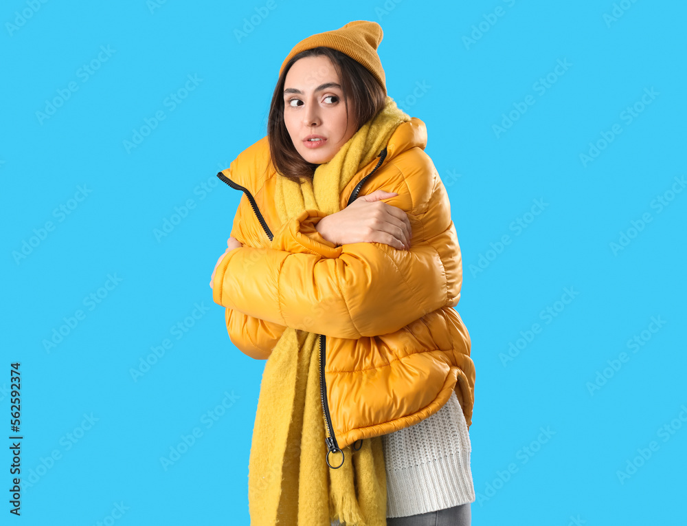 Frozen young woman in winter clothes on blue background