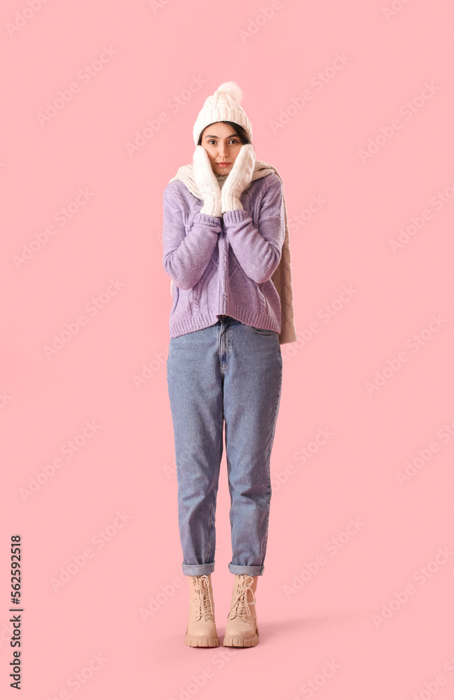 Frozen young woman in winter clothes on pink background