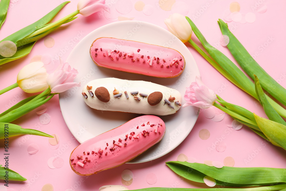 Plate with delicious glazed eclairs and tulips on pink background