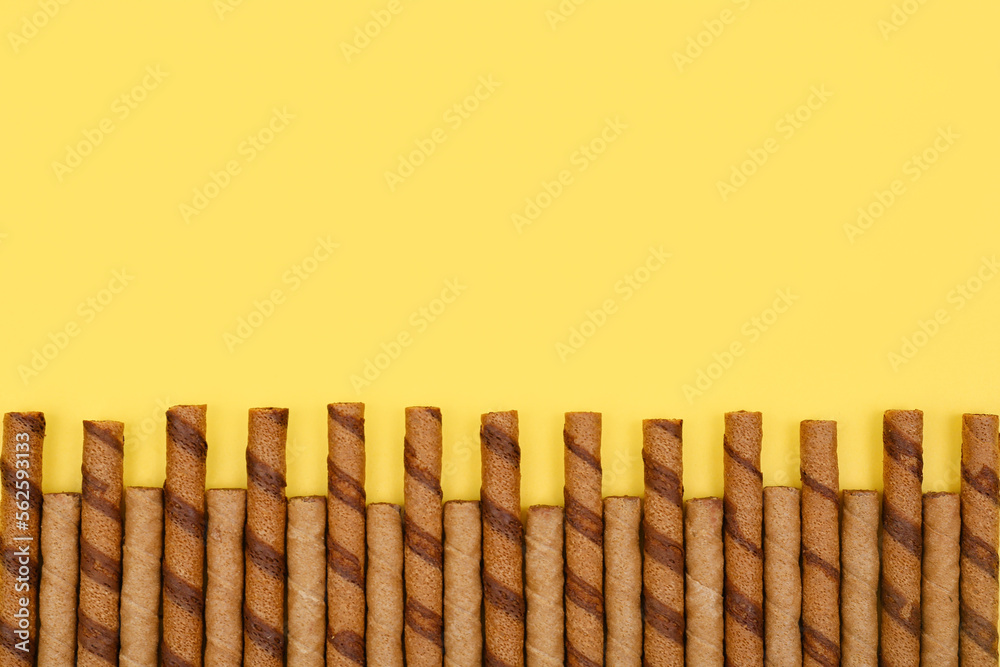 Many tasty wafer rolls on yellow background