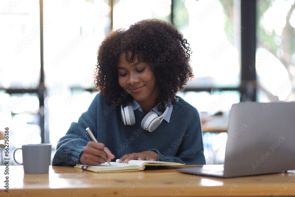 Portrait of young african woman working with laptop and reading books preparing for exams at her hom