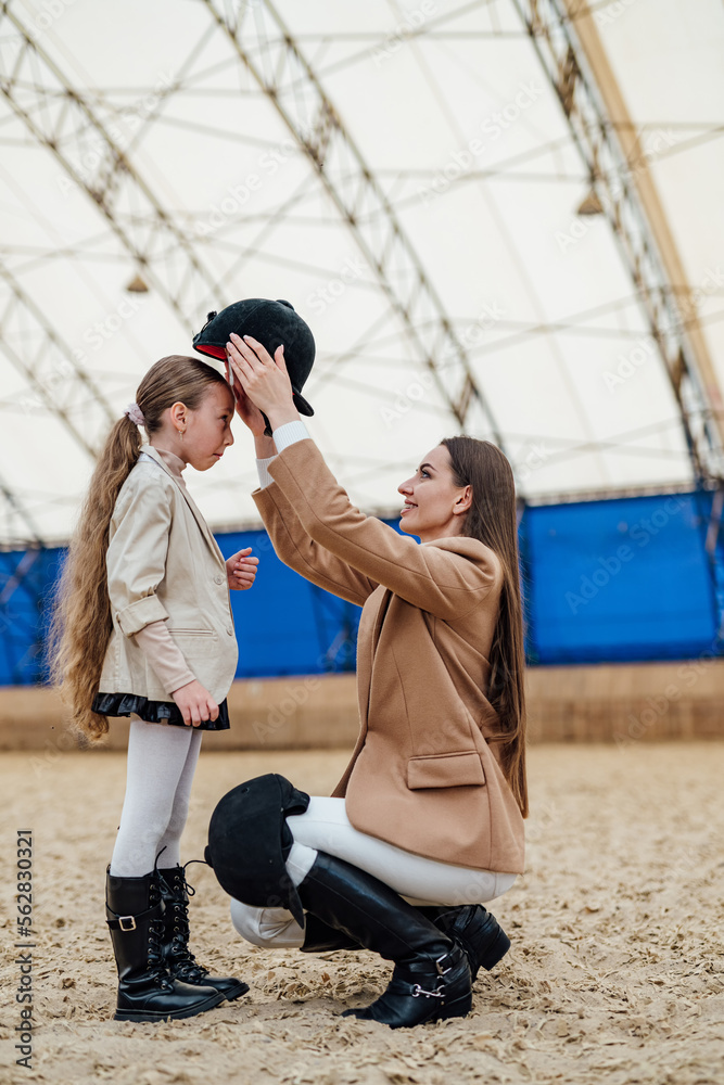 Horse lifestyle young kid with helmet. Woman equiping young girl with helmet.